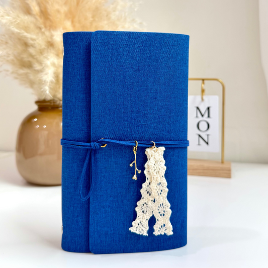 Blue fabric-bound book with decorative lace charm on a white surface with a neutral background