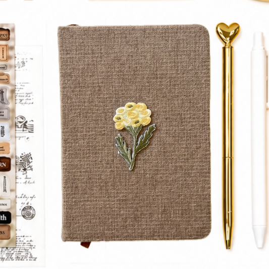 Brown notebook with a yellow flower design, gold pen, and white eraser on a white background