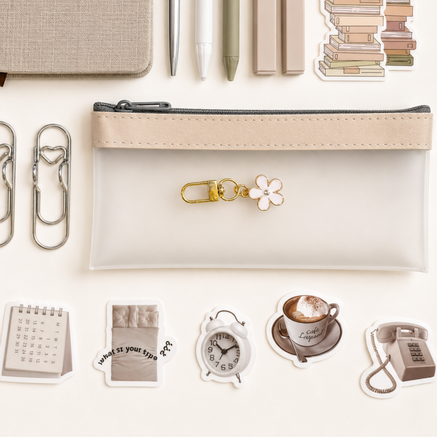 Minimalist transparent pencil pouch with neutral stationery accessories, silver paper clips, floral keychain charm and cozy vintage-inspired stickers