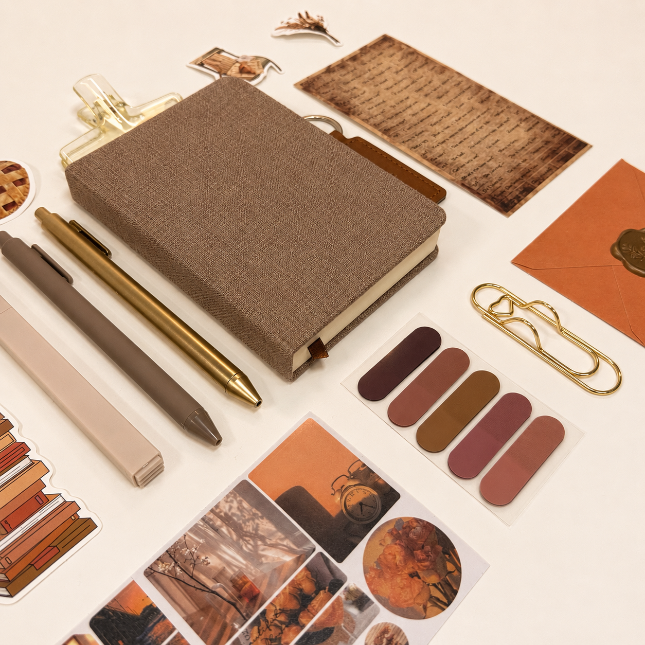 Collection of stationery items including a brown notebook, pens, and photo album on a light background
