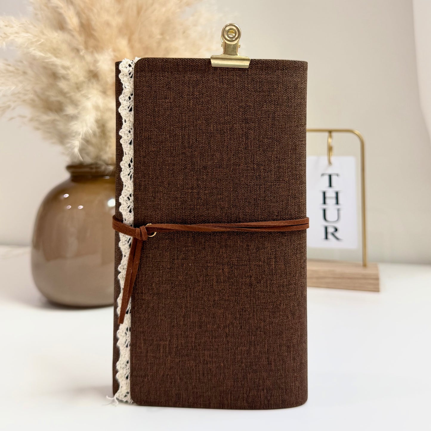 Brown textured notebook with a leather strap on a white surface with decorative elements.