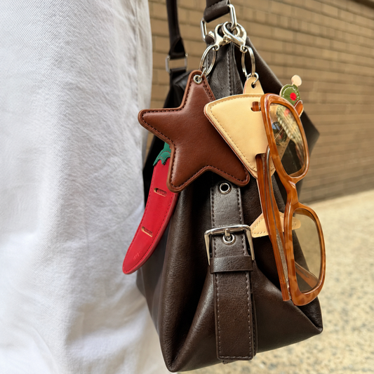 Brown leather bag with keychain, star-shaped object, and glasses attached