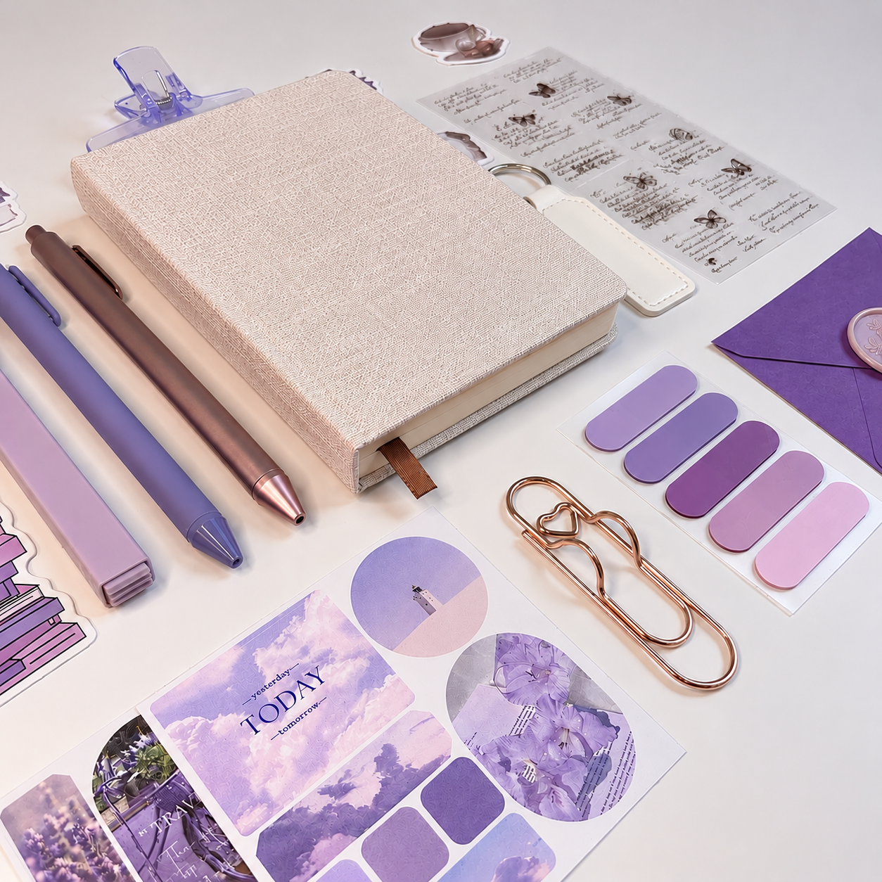 Purple stationery items including a notebook, pens, stickers, and paper clips on a white surface.
