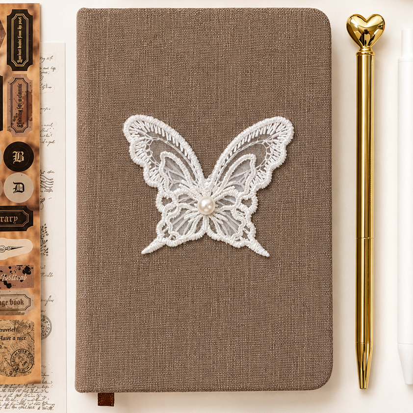 Notebook with lace butterfly design surrounded by stationery items on a white background
