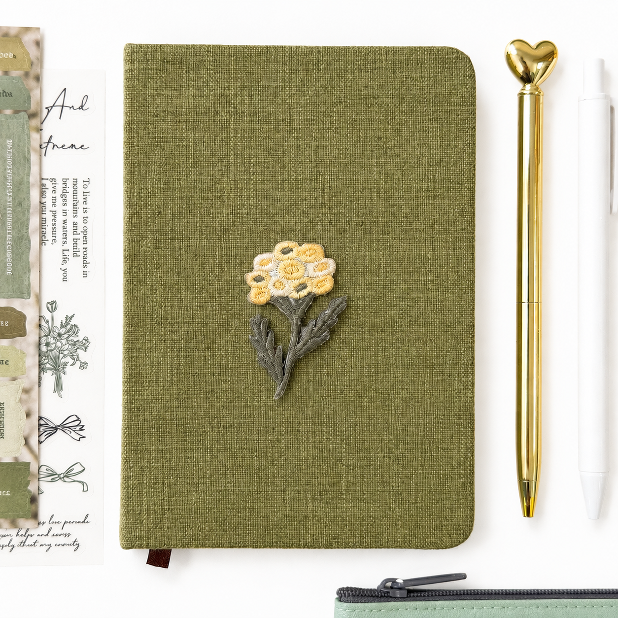 Green notebook with floral design, gold pen, and decorative item on a white background
