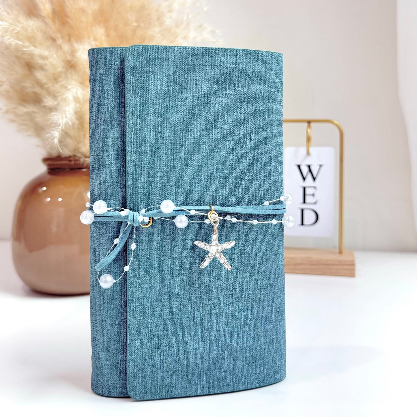 Blue textured notebook with decorative string and starfish charm on a white surface with a neutral background