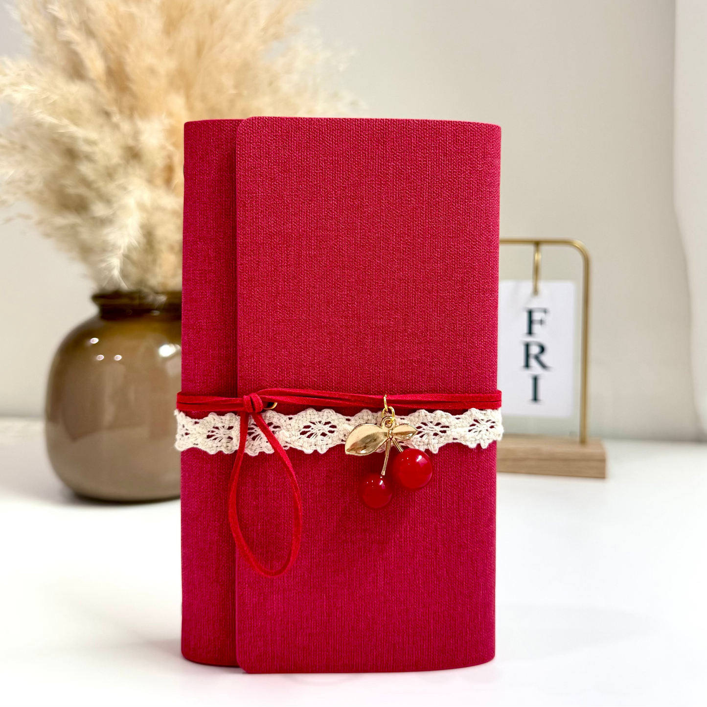 Red notebook with lace and cherry decoration on a white surface