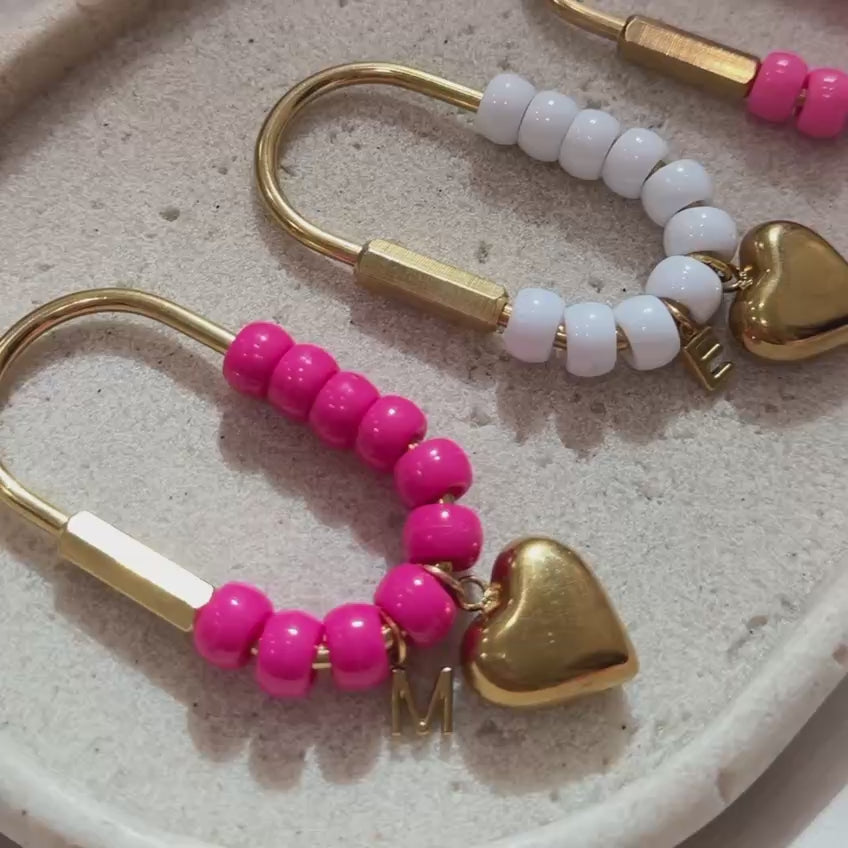 Video featuring a collection of handmade personalized heart keychains in multiple vibrant colors. Each keychain is crafted with glossy beads, gold hardware, a heart charm, and a custom initial charm. 