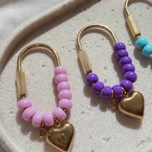 Video featuring a collection of handmade personalized heart keychains in multiple vibrant colors. Each keychain is crafted with glossy beads, gold hardware, a heart charm, and a custom initial charm. 