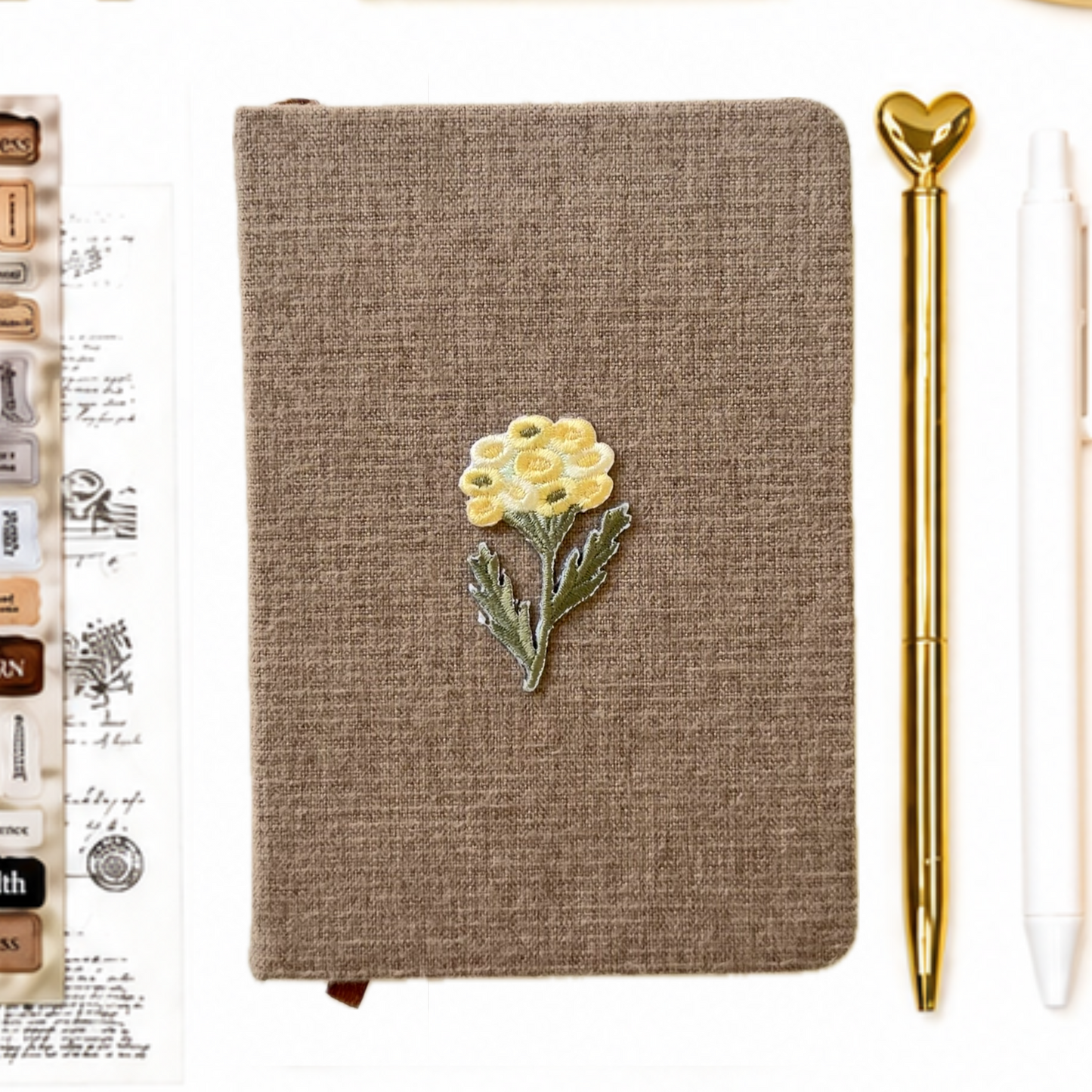 Brown notebook with a yellow flower design, gold pen, and white eraser on a white background